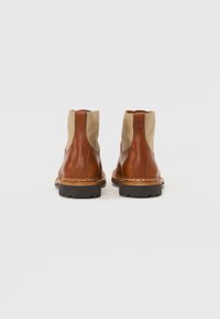 Bruine leren enkelboots met beige elastische zijpanelen, ronde neus en gestructureerde bruine rubberen zolen, met zichtbare stiksels langs de randen.