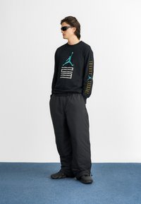 Must pikkade varrukatega särgiga, millel on teal-coloured graafika ja valged triibud; koos vaba mustade pükste ja mustade jalanõudega. Sile kangastekstuuri.