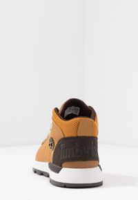 Sneaker in pelle tan e rete marrone con suola in gomma. Presenta un logo sul lato e dettagli testurizzati attorno al tallone.