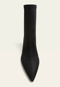 Musta kangas nilkkuri, jossa on terävä kärki, sileä pinta ja näkyvät saumarakenteet. Virtaviivainen muotoilu, jossa on tiukka siluetti.