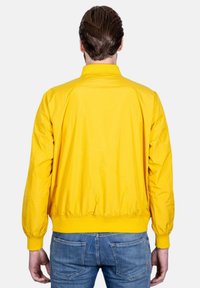 Giubbotto bomber giallo con una texture liscia, dotato di un colletto alto, polsini elasticizzati e orlo arricciato, mostrato da dietro.