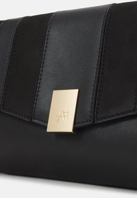 Pochette in pelle nera con pannello frontale testurizzato, chiusura in metallo dorato con logo in rilievo e design elegante e strutturato.