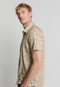 Korte mouwen overhemd van beige stof met een schelpenpatroon. Knop-down kraag en een voorpand met zwarte knopen. Casual pasvorm.
