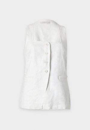 Woman wearing sleeveless white buttoned top and wide-leg white pants with square cut-out patterns, standing against plain white background.