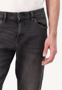 Jean en denim gris au design ajusté, avec une fermeture à bouton, des poches standard et une légère décoloration pour la texture.