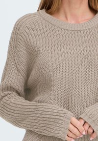 Helles beiges Strickpullover mit gerippter Textur, rundem Ausschnitt und locker sitzenden Ärmeln, mit einem entspannten Design.