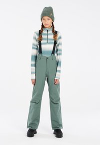 Lichtgroene skibroek met verstelbare zwarte bretels, gecombineerd met een aansluitend, gestreept longsleeve shirt en een gebreide groene beanie.