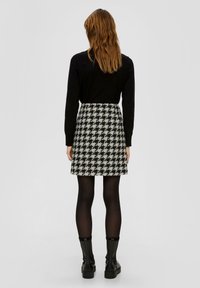 Zwart langemouwen top gecombineerd met een grijs en zwart houndstooth minirok en zwarte panty’s, afgemaakt met chunky zwarte enkellaarsjes.