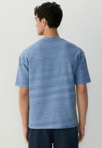 Blå stribet kortærmet t-shirt med rund hals og en afslappet pasform. Stof har en subtil tekstur med varierende nuancer af blå.
