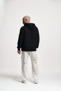Felpa nera oversize con cappuccio e coulisse, abbinata a pantaloni cargo bianchi con tasche laterali e gamba dritta.