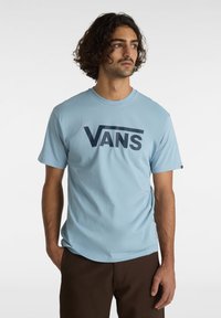 Ljusblå t-shirt i mjukt tyg, med en iögonfallande mörkblå "VANS"-logotyp över bröstet. Kort ärm och rund halsdesign.
