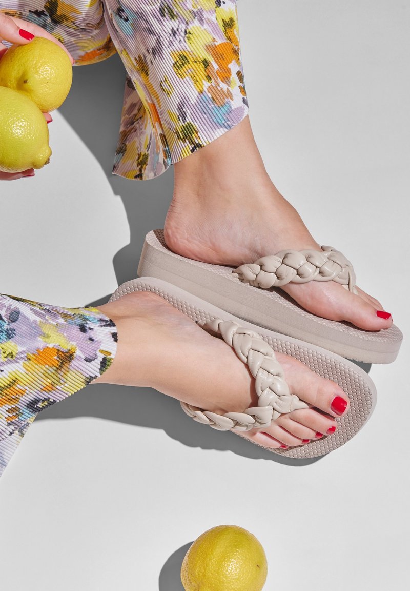 Light beige braided flip-flops with a thick sole, paired with floral-patterned pants. Lemons on a white background.