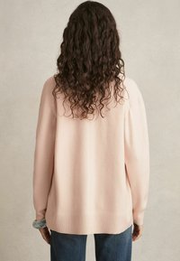 Maglione oversize rosa chiaro con una texture morbida, orlo a coste e spalle abbassate, abbinato a jeans in denim scuro. Vista posteriore mostrata.