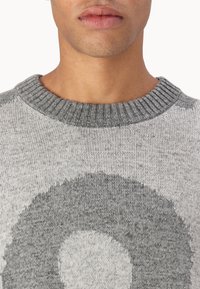 Pulover gri tricotat cu guler rotund ribat, având un model circular de culoare gri deschis. Textură moale, fără accesorii sau embellishments vizibile.