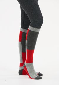 Kniestrümpfe in Rot, Grau und Schwarz mit auffälligen Farbblockmustern. Texturiertes Material mit gerippten Akzenten am oberen Rand und am Fuß.