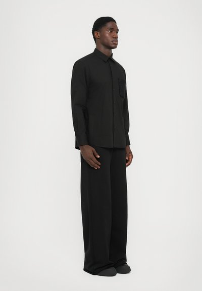 Chemise noire à boutons avec une poche texturée, accompagnée d'un pantalon noir ample. Tissu lisse et design épuré tout au long.