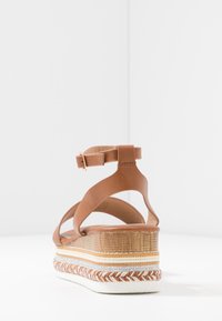 Sandale compensée en cuir marron avec une plateforme en liège stratifiée et tressée, dotée d'une bride à boucle à la cheville et d'un design à talon ouvert.