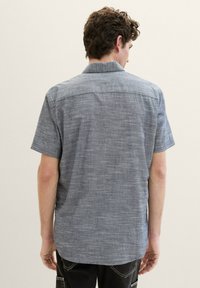Cămașă cu mânecă scurtă, cu nasturi, dintr-un material texturat de culoare albastră, cu o linie de cusătură vizibilă pe umeri și tiv rotunjit. Croi lejer.