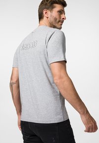 Szara koszulka z krótkim rękawem z numerem "1918" wyszytym na plecach. Wykonana z miękkiego materiału o klasycznym kroju.