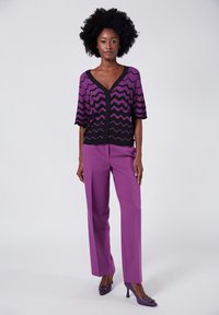 Lila zigzag-mönstrad kortärmad cardigan över matchande skräddarsydda byxor. Bärs med lila högklackade skor med utsmyckningar.