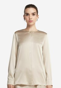 Beige långärmad blus i satinmaterial, med rund halsringning, framknappringdetalj och subtil lyster, samt en avslappnad passform.