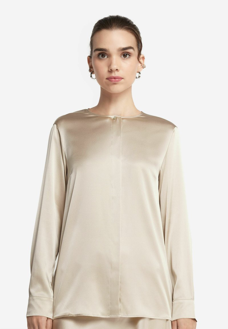 Beige långärmad blus i satinmaterial, med rund halsringning, framknappringdetalj och subtil lyster, samt en avslappnad passform.