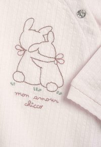 Deux lapins dessinés en contours s'enlacent avec des nœuds autour du cou, brodés sur un tissu à rayures rose clair avec le texte "mon amour doux" en dessous.