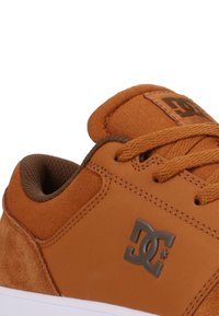 Ruskeat lenkkarit, joissa on sileä nahkaosa ja strukturoidut mokkaetailat, litteillä nauhoilla ja harmaalla logolla sivussa.