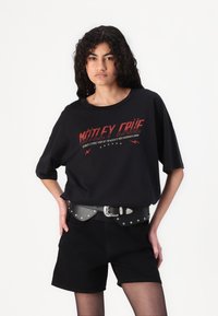 Black oversized t-shirt featuring a red graphic print, paired with high-waisted black shorts and a silver-studded black belt.
