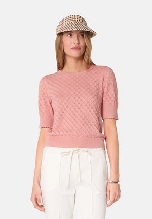 Pull court en tricot texturé rose clair avec des manches courtes et un ourlet côtelé. Une visière à carreaux complète la tenue, associée à un pantalon clair.