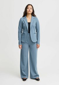 Lichtblauw pak met stippenpatroon, voorzien van een nauwsluitende blazer en wijde broek. Gemaakt van zacht materiaal, accentueert met zakken.