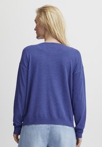 Pulover cu mânecă lungă în albastru vibrant, realizat dintr-un material moale. Dispune de o croială lejeră cu manșete și tiv din tricot, evidențiind un design simplu.