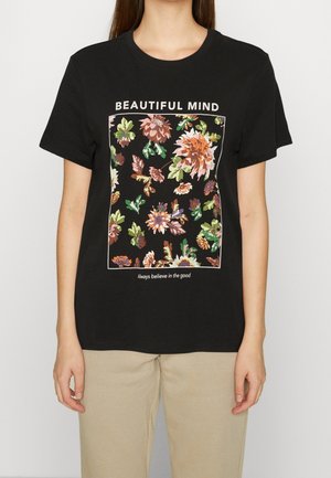 Vrouw draagt een zwart T-shirt met een bloemenprint, met de tekst "BEAUTIFUL MIND" erboven en "Always believe in the good" onder de bloemen.