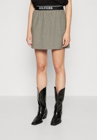 Grauer Karorock mit elastischem Bund und dem Schriftzug "HILFIGER", kombiniert mit schwarzen Leder-Cowboy-Stiefeln mit quadrater Spitze und Blockabsatz.