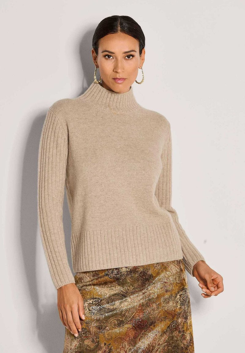 Beiger Rollkragenpullover mit geripptem Textur und langen Ärmeln, kombiniert mit einem rock mit metallischem Muster in erdigen Farbtönen und seidig schimmerndem Finish.