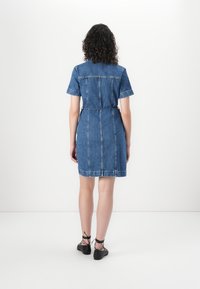Denim obleka s kratkimi rokavi, zategnjeno pasom in A-linijo. Dopolnjena z ravnim robom in vidnimi šivi. Črne čipkane čevlje.