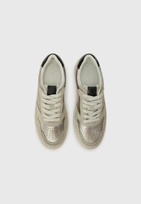 Sneaker in pelle beige con accenti metallici argento, punta perforata, lacci piatti e dettagli neri sul tallone. Design casual e leggero.