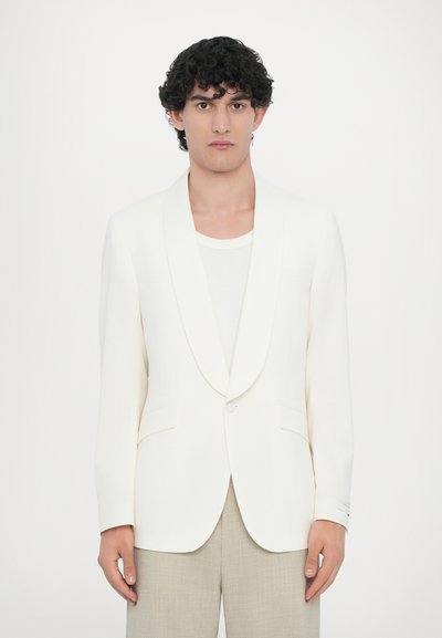 Weiße Blazer mit Schalkragen, Ein-Knopf-Verschluss, zwei Fronttaschen, glatte Textur, kombiniert mit hellbeigen Hosen.