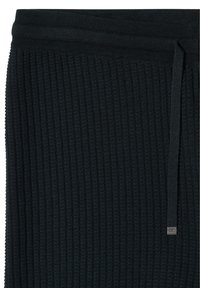 Tissu tricoté côtelé noir avec un cordon et une étiquette métallique sur le côté droit, probablement une partie de la taille ou du poignet d'un vêtement.