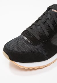 Schwarzer Sportschuh aus Mesh- und Wildledermaterialien. Verfügt über ein strukturiertes Obermaterial, flache Schnürsenkel und eine Gummisohle mit einem braunen Akzent.