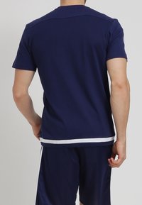 Granatowy t-shirt z krótkim rękawem, gładka tkanina, okrągły dekolt, biały pasek na dole, widok od tyłu pokazujący luźny krój i prosty design.