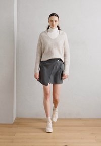 Lys beige V-hals genser, svart skjørt med omslagsdesign, og hvite joggesko. Genseren er myk, skjørtet har en glatt tekstur og minimalistisk stil.