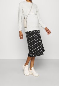 Top de manga larga gris claro, falda negra con lunares blancos y zapatillas ligeras. Incluye un pequeño bolso ligero con tira cruzada.