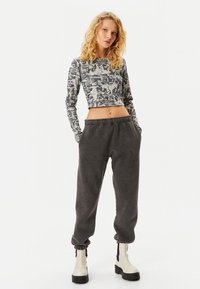 Grijs cropped longsleeve shirt met grafische print, gecombineerd met donkergrijze sweatpants met een elastische tailleband en off-white enkellaarzen.
