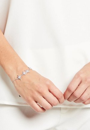 Bracciale d'argento con elementi a forma di stella, collegati da una delicata catena, su uno sfondo chiaro, indossato su una mano con un tono di pelle naturale.