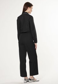 Maglietta nera aderente con maniche lunghe e polsini a bottone, abbinata a pantaloni neri a gamba larga. Presenta scarpe metallizzate argento come accento.