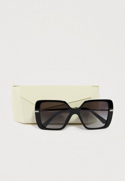 Sorte oversize solbriller med graduerede linser, firkantet form og sølvdetaljer på stellets arme, placeret i et cremefarvet etui.