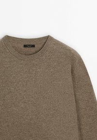 Pull en maille marron clair avec un col rond. La texture est douce et tissée, présentant un motif lisse et uniforme ainsi qu'une coupe décontractée.