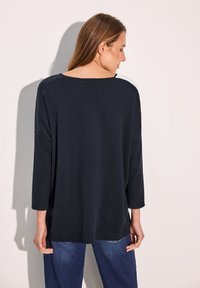 Schwarzes, leichtes Strickoberteil mit langen Ärmeln, breitem Halsausschnitt und gerippten Akzenten an den Ärmeln, von hinten gezeigt.