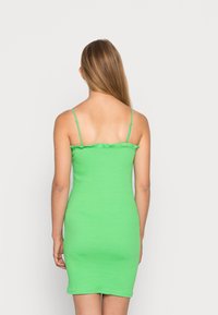 Vestido mini verde elegante, com riscas, alças finas e um detalhe de decote em babados. Silhueta ajustada, textura suave e cor sólida em toda a peça.